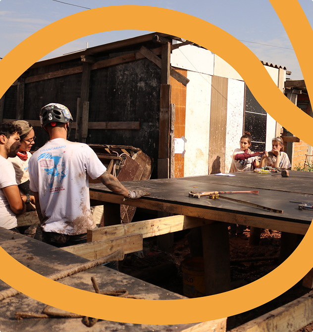 Imagem de pessoas sentadas em frente a uma das mesas do coworking do Galpão ZL. Elas conversam sobre o plano de ação para a construção das casas do projeto +Lapena Habitar.