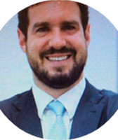 Imagem de Guilherme Setubal Souza e Silva. Ele tem cabelos na tonalidade castanho-escura e barba. Guilherme aparece usando terno azul-marinho, gravata azul-clara e está à frente de uma parede.