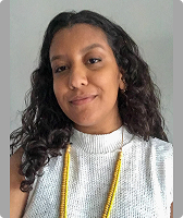 Imagem de Sthefani Domenica Pedroso. Ela tem cabelos cacheados na altura do ombro, usa blusa regata na cor branca e colar amarelo. Domenica aparece à frente de uma parede branca.