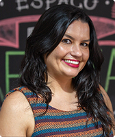 Imagem de Andrelissa Teressa Ruiz. Ela tem cabelos escuros longos e usa blusa regata colorida com listras horizontais nas cores vinho, laranja, amarelo e azul. Andrelissa aparece sorrindo e está à frente de uma parede preta com pinturas feitas com giz.