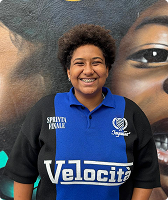 Imagem de Sara Estela Pereira Correa. Sara tem cabelo crespo com corte black power. Ela aparece na foto sorrindo, usando uma camiseta polo nas cores azul e preta e à frente de uma parede na qual há o desenho do rosto de uma mulher negra.