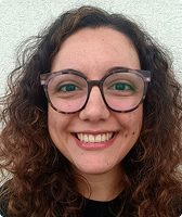 Imagem de Anne Caroline Barreto. Ela tem cabelos encaracolados e usa óculos de acetato e blusa na cor preta.