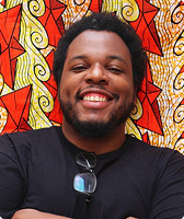 Imagem de Uvanderson Vitor da Silva. Ele tem cabelo curto em formato black power e aparece sorrindo, em frente a uma parede com desenhos nas cores amarela e vermelha. Uvanderson usa uma camiseta preta, à qual há um par de óculos presos.