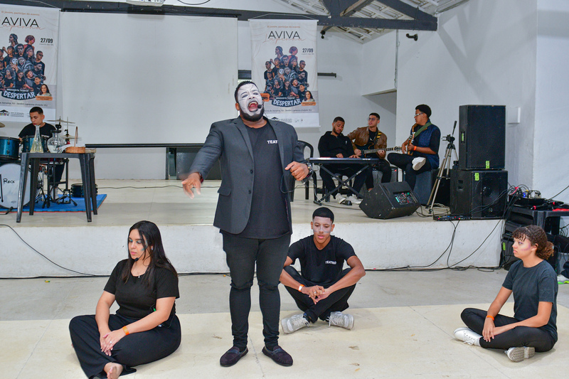 Intervenção teatral no Aviva Lapenna com performance de homem maquiado de branco cantando no centro do palco.