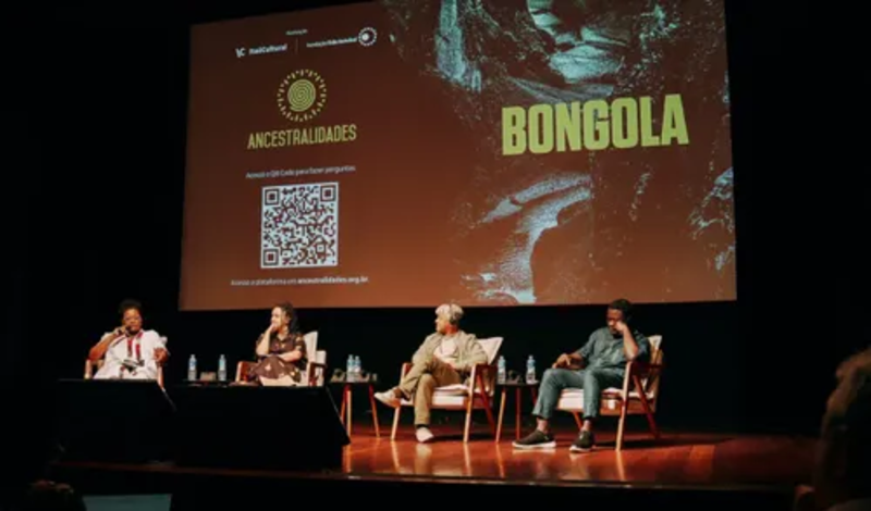 Palco do auditório do Itaú Cultural com participantes do evento Bongola diante de tela com título, logo e QR Code.