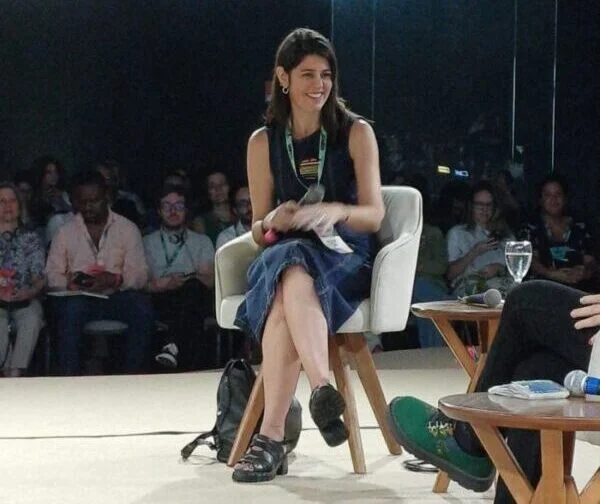 Mariana Almeida sentada em cadeira durante o 13º Congresso Gife, com plateia ao fundo.