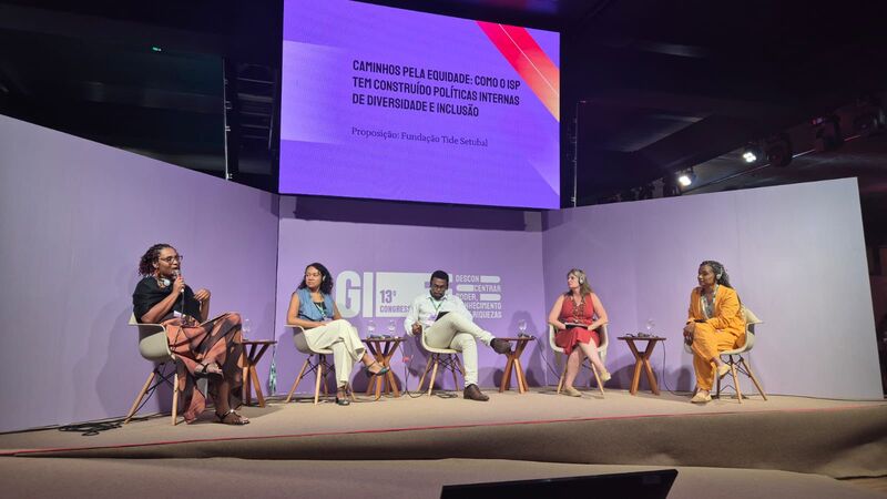 Viviane Soranso com participantes de mesa em pe e abracados diante de tela com logos institucionais.