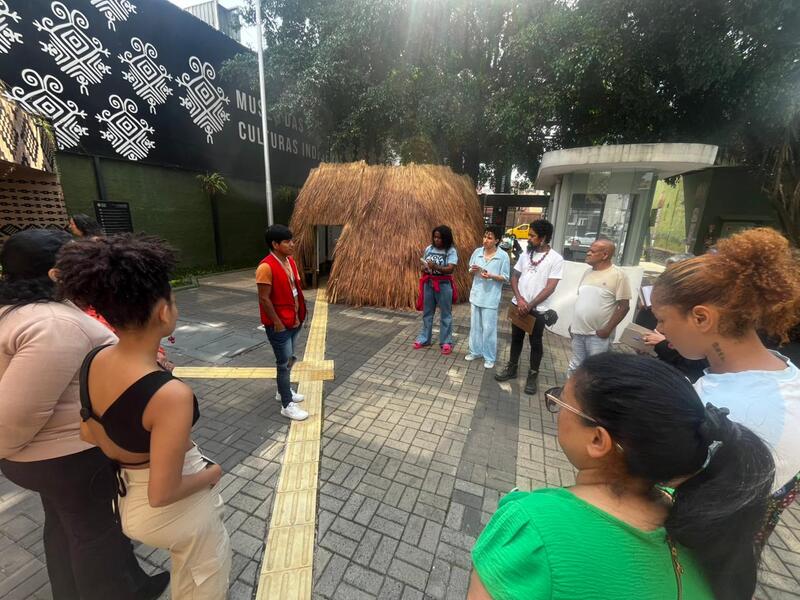 Equipe do projeto Primeiras Embarcações em área externa do Museu da Cultura Indígena, reunida em roda ouvindo orientações.