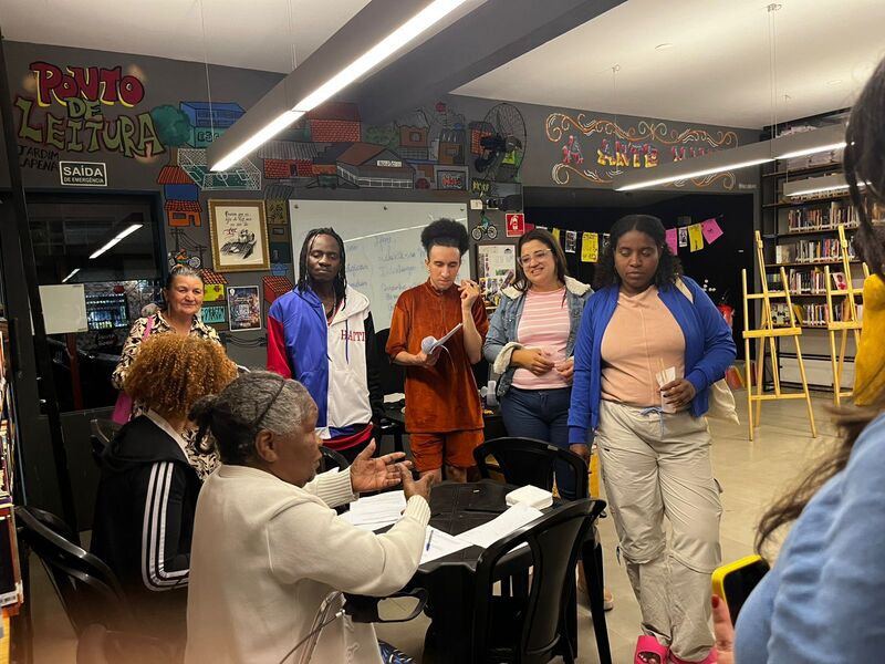 Participantes do projeto Primeiras Embarcações ouvindo orientações de Dona Gloria no Ponto de Leitura do Jardim Lapena.