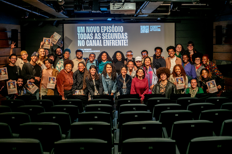 Grupo com participantes das coletivas e público reunidos diante da tela do auditório do Itaú Cultural.