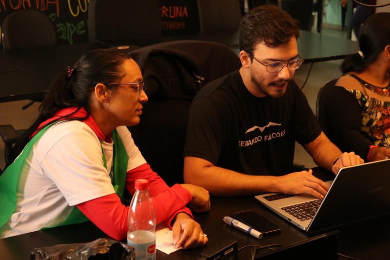 A imagem mostra duas pessoas conversando sobre o plano de ação para o projeto +Lapena Habitar - uma delas usa um notebook e mostra informações visíveis nesse mesmo equipamento.