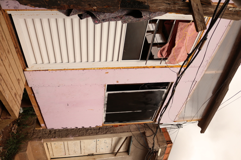 Casa do projeto +Lapena Habitar construída sobre palafitas, com placas na cor rosa, ao lado de uma casa de alvenaria.