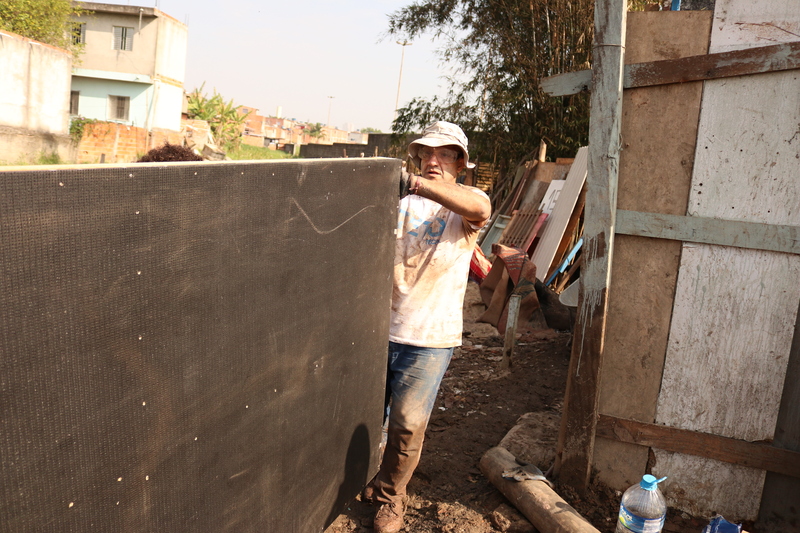 Homem com óculos de proteção e capacete de construção carregando material para obra no projeto +Lapena Habitar.