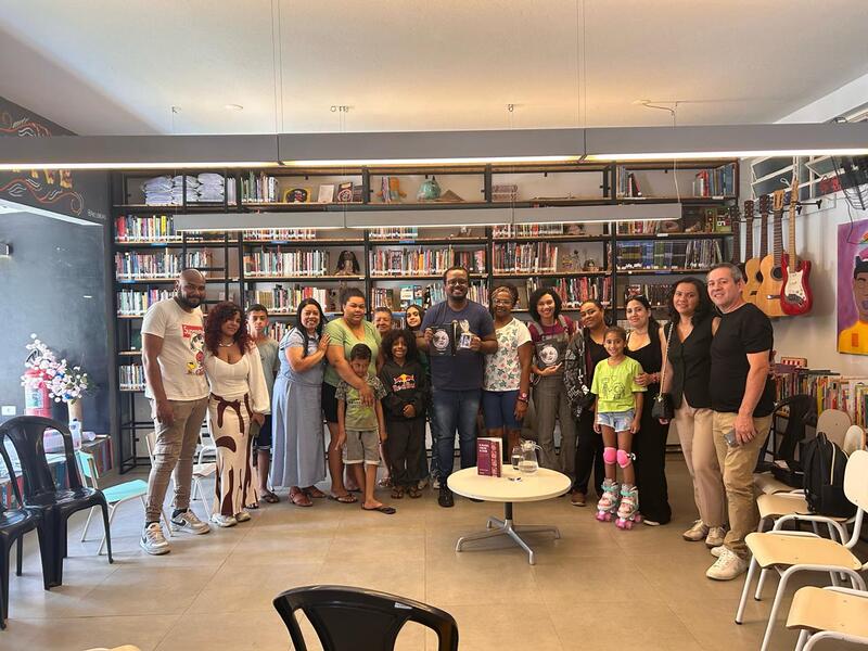 Imagem do lançamento do livro Viagem ao Cinema Mudo, de Rodrigo Veninno. Aparecem 17 pessoas, inclusive crianças, à frente de uma estante com livros. O autor está ao centro e segura um exemplar da obra.