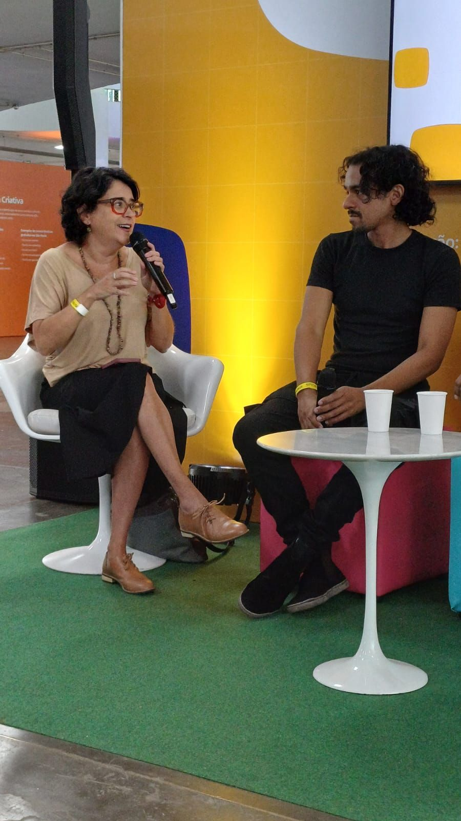 Fernanda Nobre falando ao microfone ao lado de Frances Gonf durante o evento Trampos do Futuro.